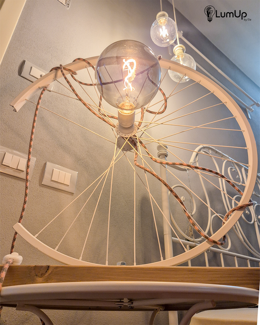 Lampada artigianale realizzata con ruota di bicicletta e legno di recupero.
Colore Bianco - Lampadina stile vintage - Cavo elettrico rosa e salvia - immagine intera