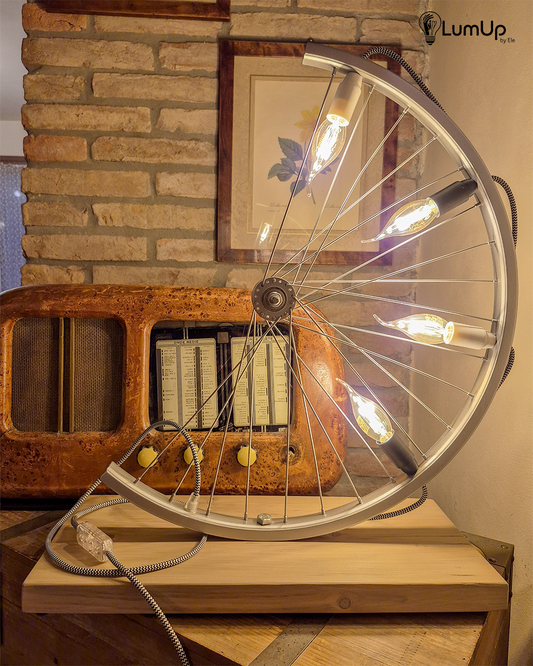 Lampada artigianale realizzata con ruota di bicicletta e legno di recupero.
Colore Argento - Lampadine stile vintage - Cavo elettrico bianco e nero - immagine intera