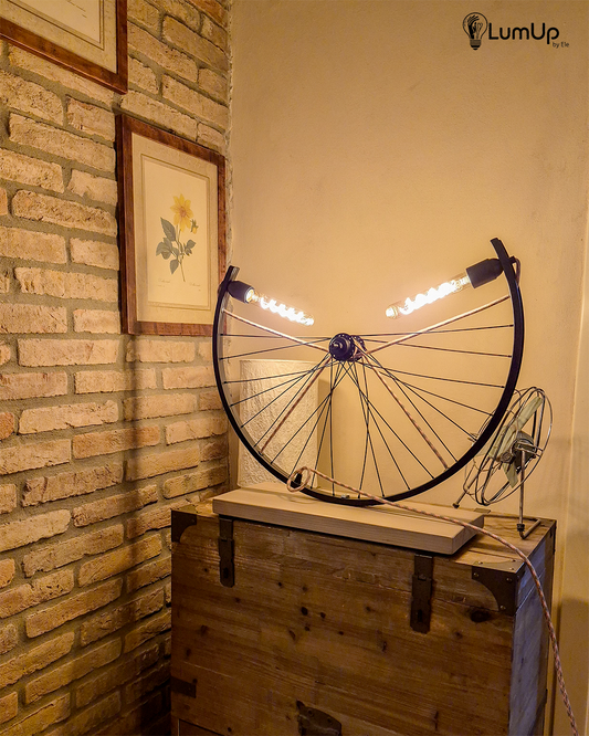 Lampada artigianale realizzata con ruota di bicicletta e legno di recupero.
Colore Nero - Lampadine stile vintage - Cavo elettrico rosa e salvia - immagine intera