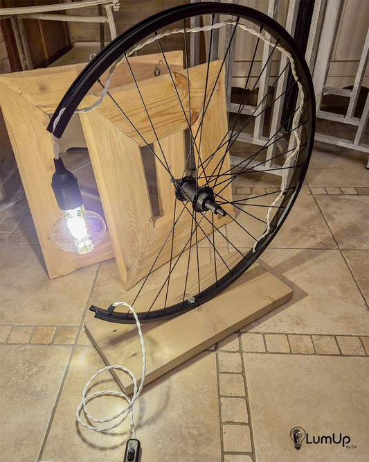 Lampada artigianale realizzata con ruota di bicicletta e legno di recupero.
Colore Nero - Lampadina stile vintage - Cavo elettrico bianco trecciato - immagine intera