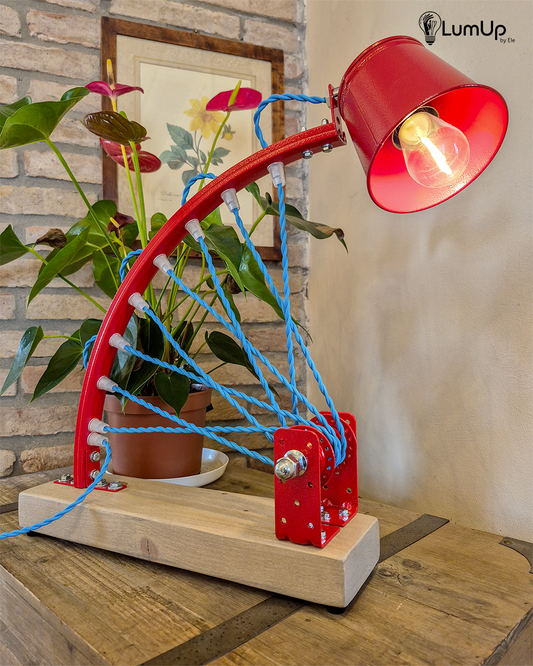Lampada artigianale realizzata con parte di ruota di bicicletta e legno di recupero.
Colore Rosso - Cavo tessile azzurro trecciato - Punto luce snodato - immagine intera
