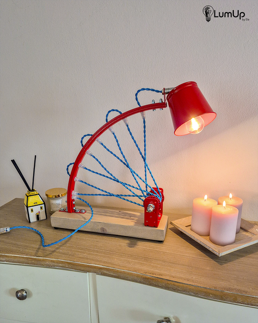 Lampada artigianale realizzata con parte di ruota di bicicletta e legno di recupero.
Colore Rosso - Cavo tessile azzurro trecciato - Punto luce snodato - immagine intera