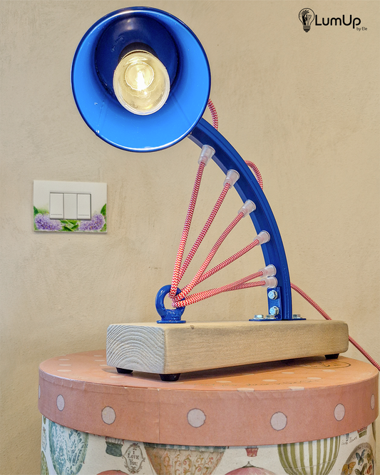 Lampada artigianale realizzata con parte di ruota di bicicletta e legno di recupero.
Colore Blu - Cavo tessile rosso e bianco - Punto luce snodato - immagine intera