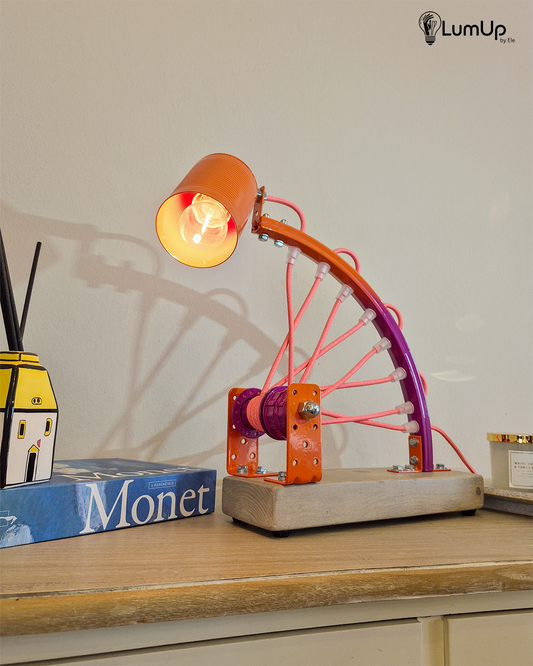 Lampada artigianale realizzata con parte di ruota di bicicletta e legno di recupero.
Colore Arancione e viola - Cavo tessile rosa e giallo - Punto luce snodato - immagine intera