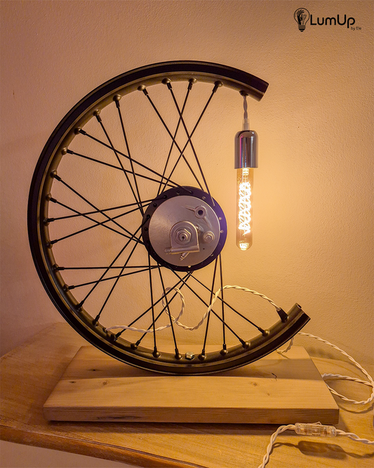 Lampada artigianale realizzata con ruota di motocicletta e legno di recupero.
Colore Nero - Lampadina stile vintage - Cavo elettrico bianco trecciato - immagine intera