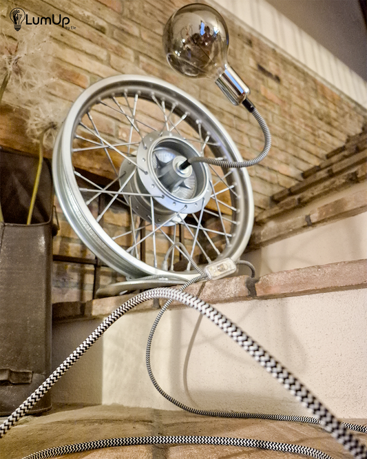 Lampada artigianale realizzata con ruota di motocicletta e base metallica.
Colore Argento - Lampadina stile vintage - Braccio modellabile - Cavo elettrico bianco e nero - immagine intera