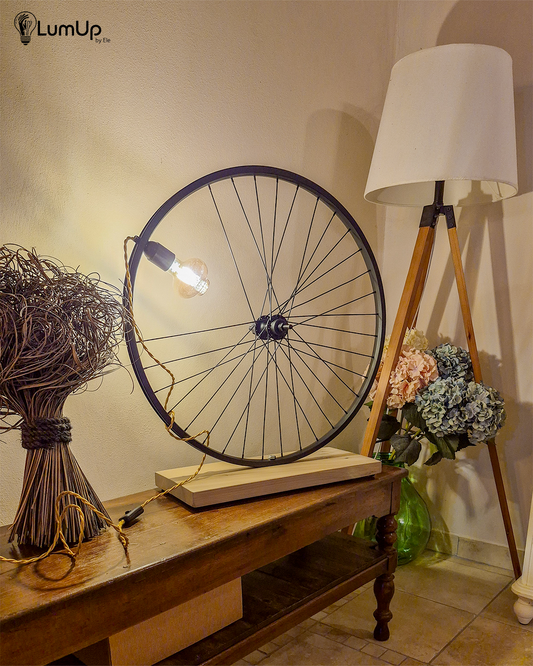 Lampada artigianale realizzata con ruota di bicicletta e legno di recupero.
Colore Nero - Lampadina stile vintage - Cavo elettrico oro trecciato - immagine intera